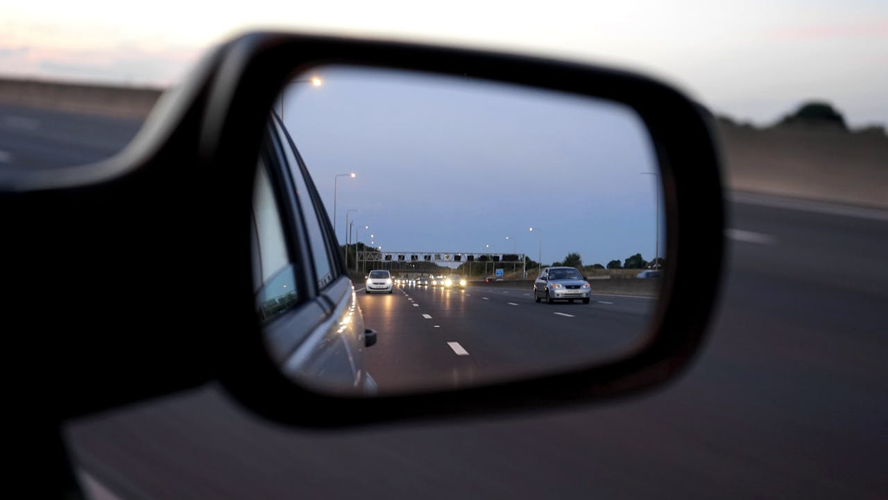 Home View of cars on the highway reflected in a vehicles side mirror at twilight, capturing motion and speed.